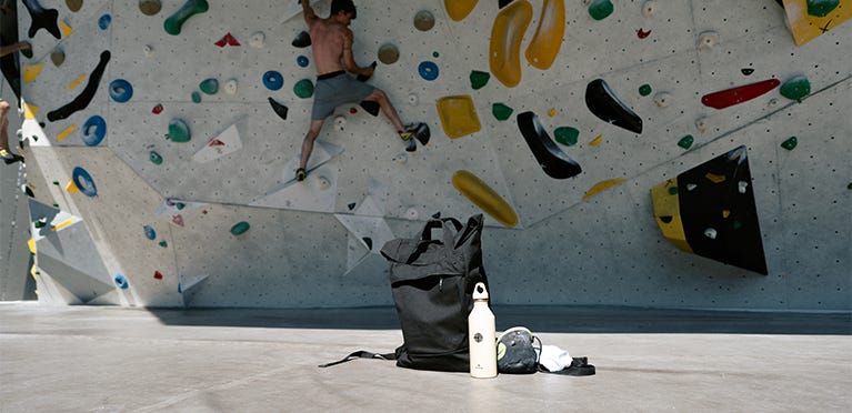 Mann klettert an Boulderwand, eoto Rucksack im Vordergrund