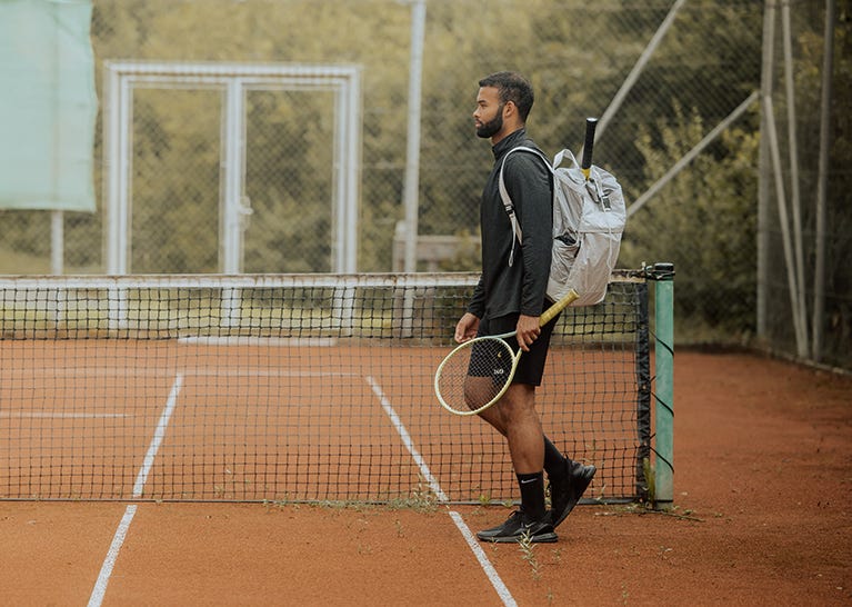 eoto Rucksack für den Sport Mann läuft mit Schläger und eoto Rucksack auf Tennisplatz
