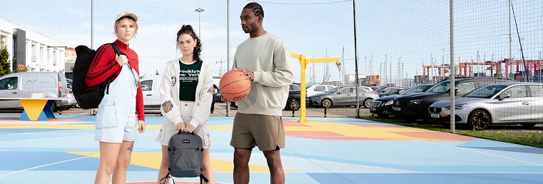 3 Personen stehen mit Daypacks und einem Basketball auf dem Sportplatz