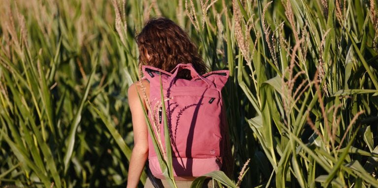 Frau mit rosanem eoto Rucksack läuft durch Feld