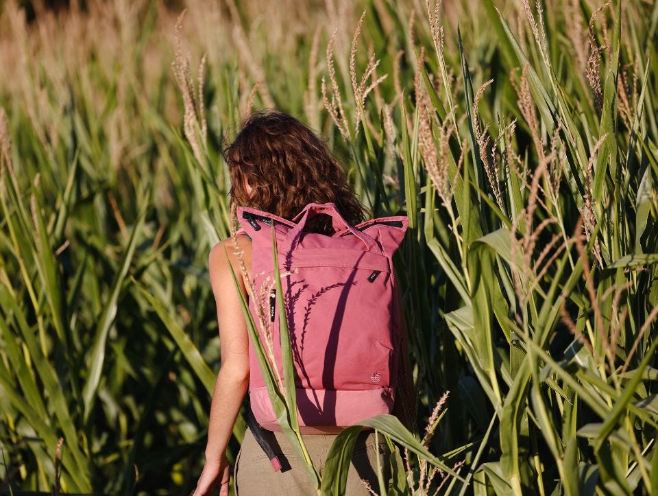 Frau mit rosanem eoto Rucksack läuft durch Feld